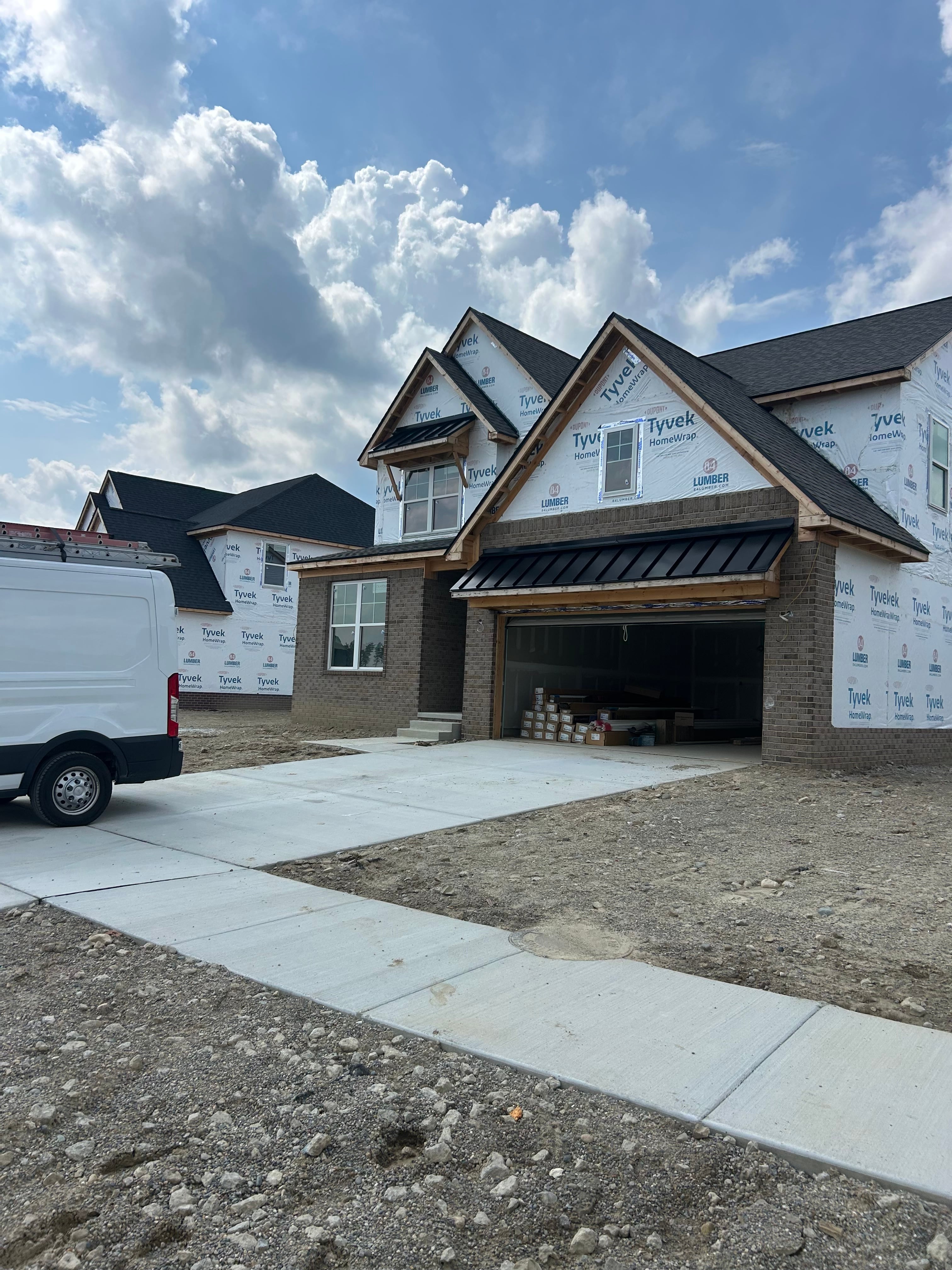 New construction home mid-build with dark navy standing seam metal roofing panels installed, Tyvek housewrap on exterior walls, navy board-and-batten siding accents, white windows, and JD Contracting crew on site in Oakland County